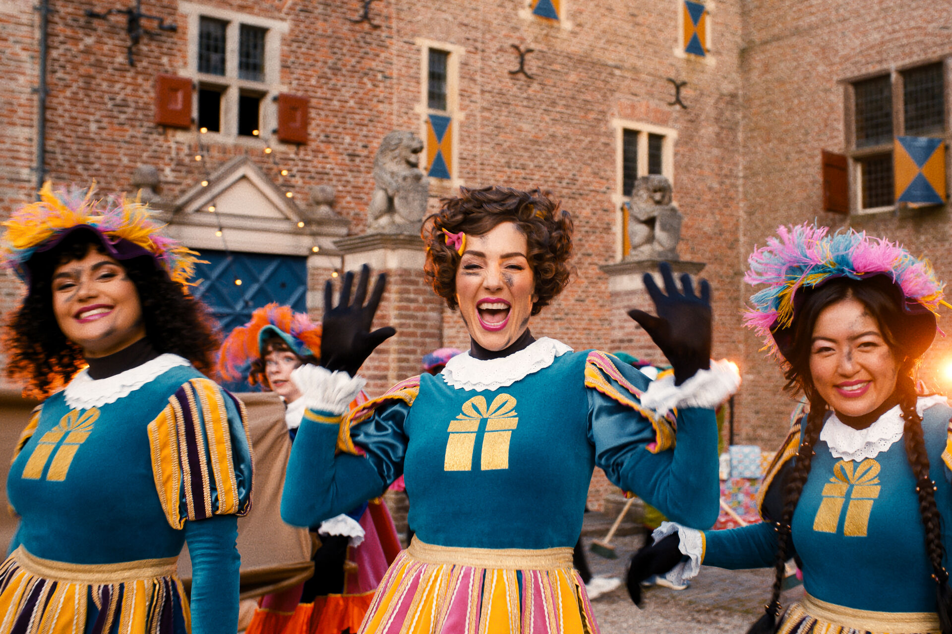 Drie KADO-pieten in cadeau-jurken poseren lachend voor het kasteel van Sinterklaas